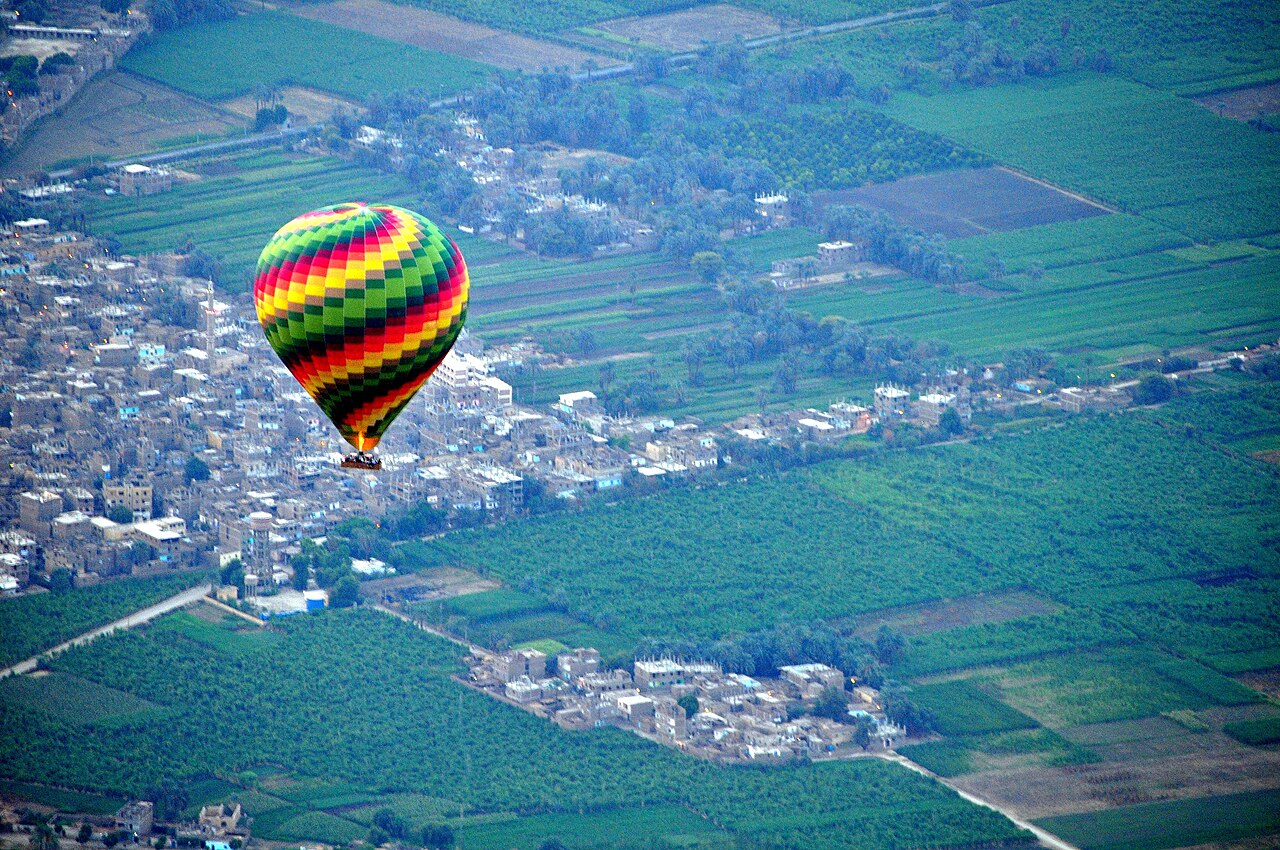 A colourful hot air balloon floating above Luxor's patchwork of green fields