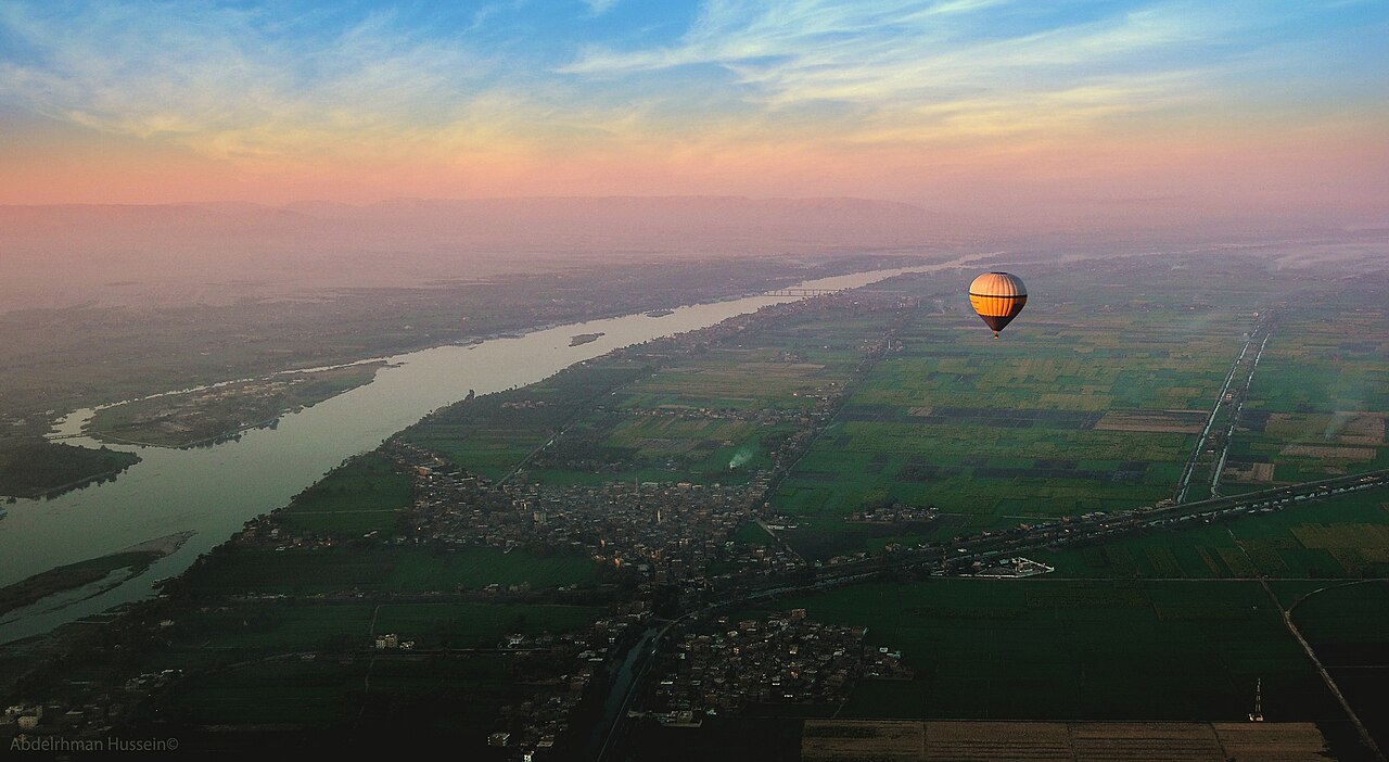 A hot air balloon floating beside the Nile at sunrise